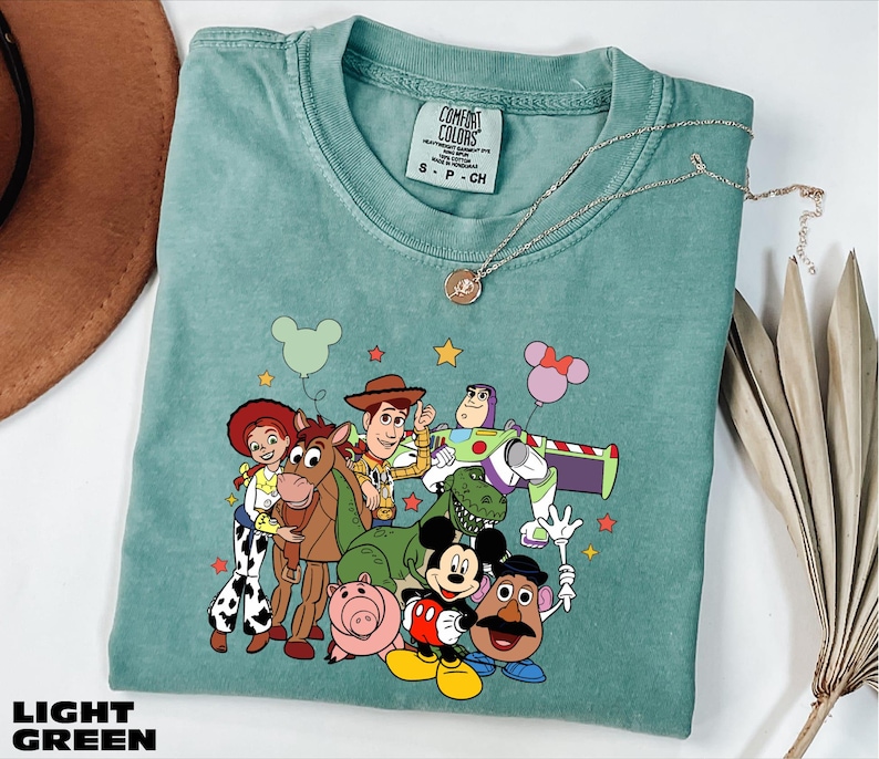 A light blue t-shirt with a colorful graphic of characters from the Toy Story movie, including Woody, Buzz Lightyear, and other beloved characters.