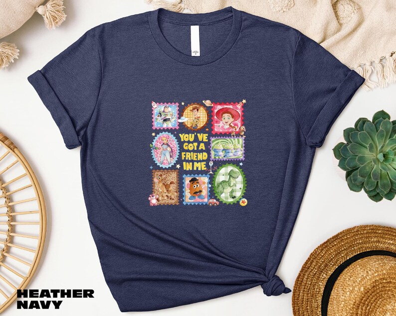 A navy blue t-shirt with a collage of colorful images and text, including characters from the Toy Story franchise, along with the text "You've got a friend in me".
