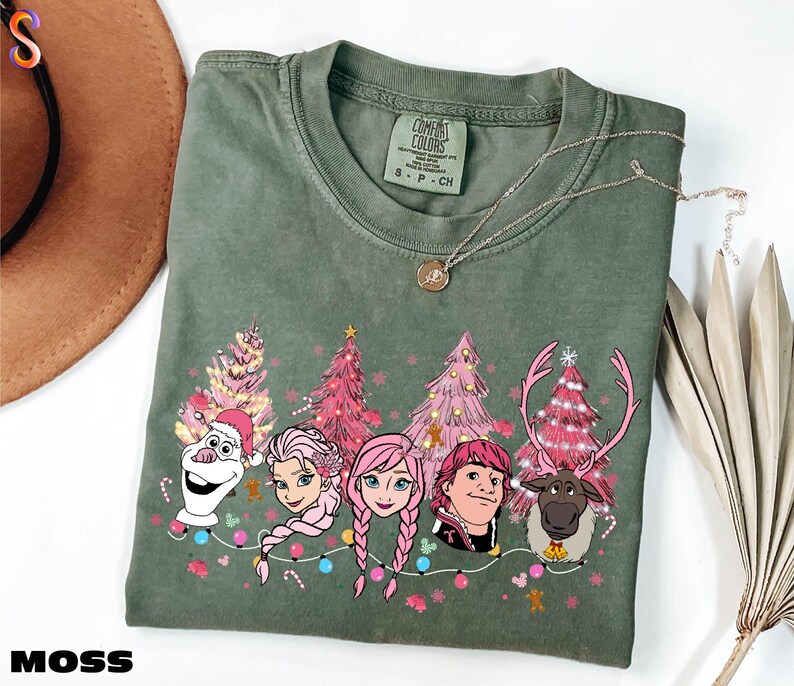 A green t-shirt with a Christmas-themed design featuring characters from the Disney movie Frozen, including Olaf, Elsa, Anna, and other popular characters.