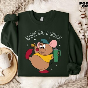 K&ouml;nnte beinhalten: Dunkelgr&uuml;nes Sweatshirt mit einer Cartoon-Maus, die ein Getr&auml;nk und ein St&uuml;ck K&auml;se h&auml;lt. Der Text "lookin' like a snack" ist in Wei&szlig; geschrieben. Das Sweatshirt hat lange &Auml;rmel und einen Rundhalsausschnitt.