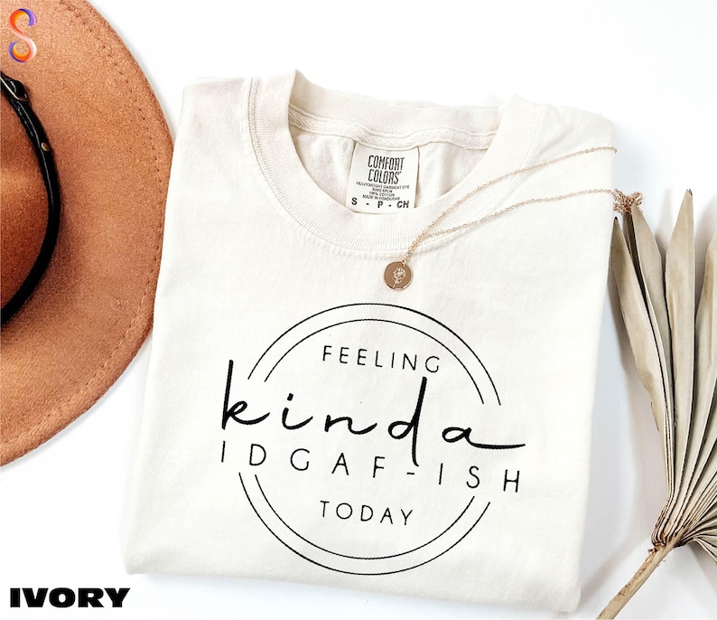 a white t-shirt with a black text design that reads "Feeling kinda idgafish today", accompanied by a brown hat and a plant.