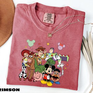 A red t-shirt with a cartoon character design featuring characters from the Toy Story franchise, including Woody, Buzz Lightyear, and other beloved characters.
