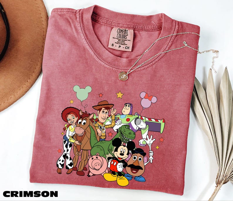 A red t-shirt with a cartoon character design featuring characters from the Toy Story franchise, including Woody, Buzz Lightyear, and other beloved characters.