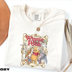 A white t-shirt with a Winnie the Pooh graphic printed on it, along with a necklace and some decorative elements.