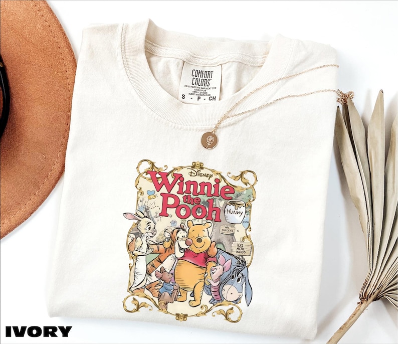 A white t-shirt with a Winnie the Pooh graphic printed on it, along with a necklace and some decorative elements.