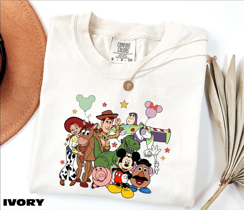 A white t-shirt with a colorful graphic of characters from the Toy Story movie, including Woody, Buzz Lightyear, Lassie, and other beloved characters.
