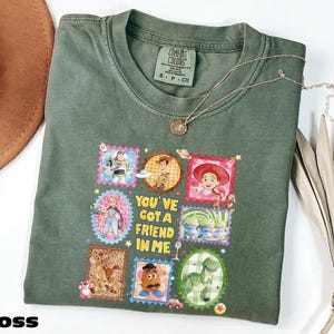 A green t-shirt with a colorful graphic design featuring characters from the Toy Story movie, along with the text "You've got a friend in me".