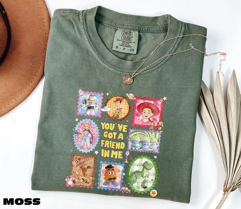 A green t-shirt with a colorful graphic design featuring characters from the Toy Story movie, along with the text "You've got a friend in me".