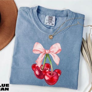 a blue shirt with a pink bow and two cherries on it