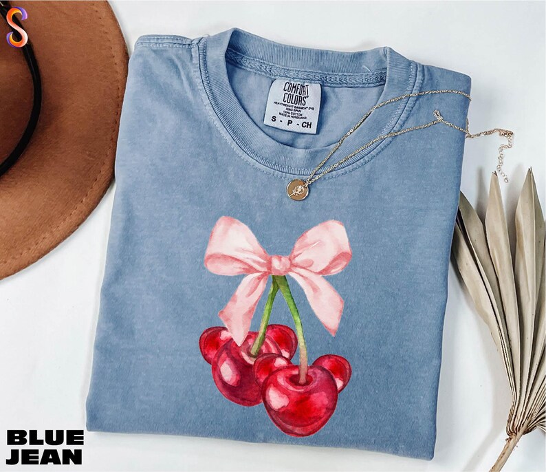 a blue shirt with a pink bow and two cherries on it