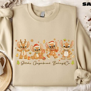 A beige sweater with a graphic design featuring four cartoon characters, including Stitch, Gingerbread, Baking, and Cookie, along with the text "Stitch's Gingerbread Baking Co."