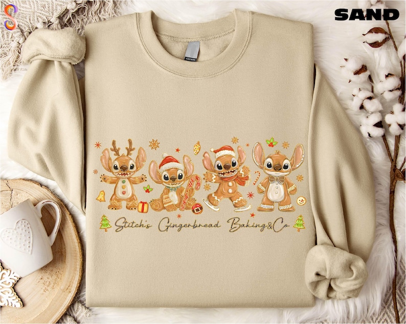 A beige sweater with a graphic design featuring four cartoon characters, including Stitch, Gingerbread, Baking, and Cookie, along with the text "Stitch's Gingerbread Baking Co."