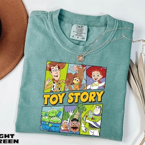 A green t-shirt with a colorful graphic of characters from the Toy Story movie, including Woody, Buzz Lightyear, and other beloved characters, is displayed on a white surface.