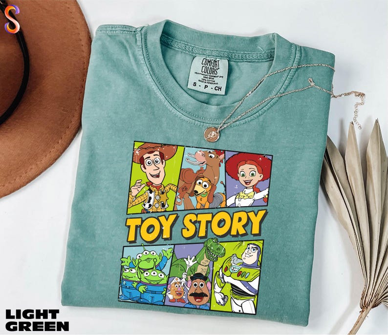 A green t-shirt with a colorful graphic of characters from the Toy Story movie, including Woody, Buzz Lightyear, and other beloved characters, is displayed on a white surface.