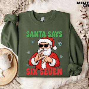 A green sweatshirt with a cartoon Santa Claus and the text "Santa says six seven" printed on it, along with snowflakes and a mug.