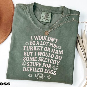A green t-shirt with a humorous text printed on it, along with a necklace and some decorative leaves.