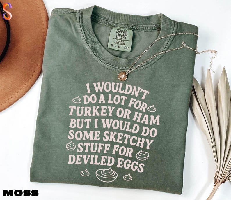 A green t-shirt with a humorous text printed on it, along with a necklace and some decorative leaves.