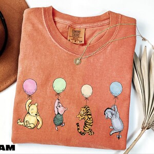 a red t-shirt with a cartoon illustration of Winnie the Pooh and his friends holding balloons.