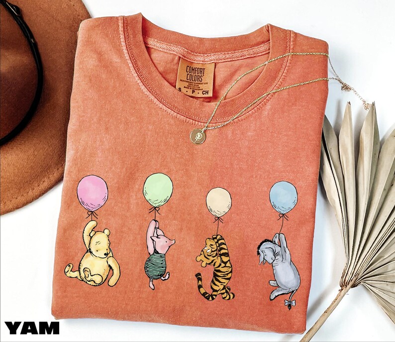 a red t-shirt with a cartoon illustration of Winnie the Pooh and his friends holding balloons.