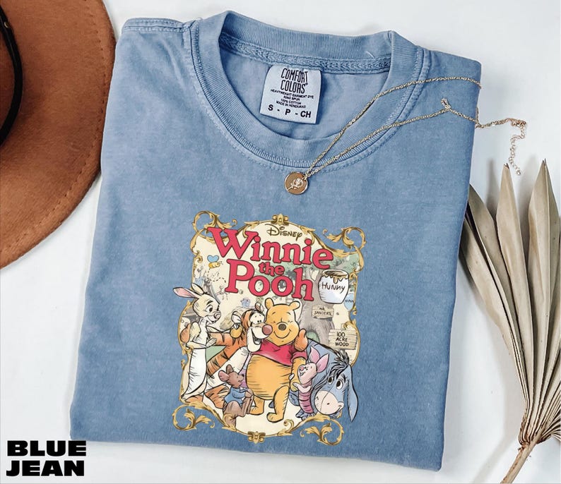 A blue t-shirt with a Winnie the Pooh graphic and a necklace are displayed on a white surface.