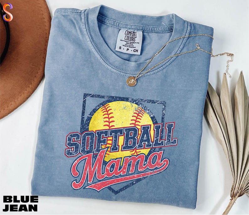 A blue softball-themed t-shirt with the text "SOFTBALL MAMA" printed on it, along with a necklace and a brown hat.