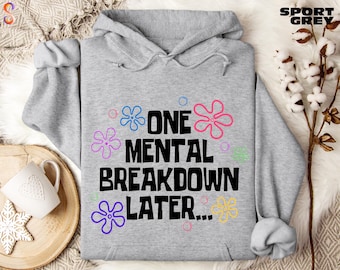 May include: A light gray hooded sweatshirt featuring the black text ONE MENTAL BREAKDOWN LATER... surrounded by colorful flower outlines in blue, pink, purple, green, and yellow, with the words SPORT GREY printed in the top right corner.
