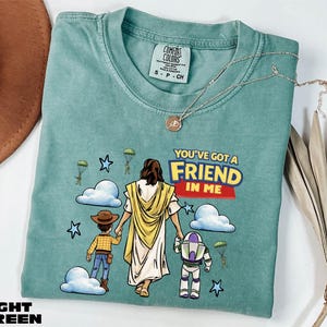 A green t-shirt with a cartoon illustration of a person holding a Bible and a child, along with a message that says "You've got a friend in me".