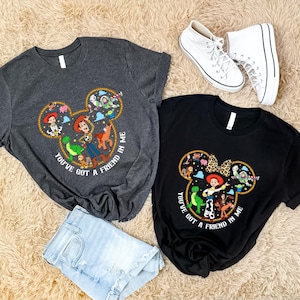 a pair of t-shirts with Disney characters and a pair of white sneakers, all laid out on a beige carpet.