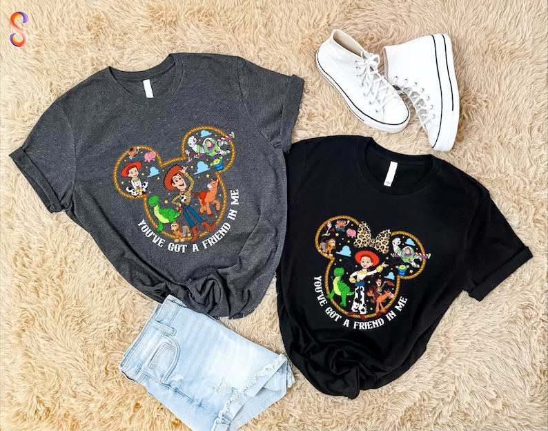 a pair of t-shirts with Disney characters and a pair of white sneakers, all laid out on a beige carpet.