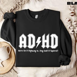 May include: Black sweatshirt with the white text "AD+HD" and a lightning bolt graphic. Below the text is the phrase "We're On A Highway to... Hey Look! A Squirrel!" The word "BLACK" is in the upper right corner.