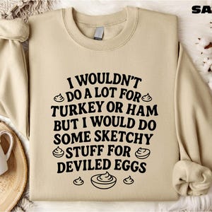 A beige sweatshirt with a humorous text printed on it, along with a mug and some decorative elements like a branch and a bowl.