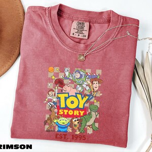 A red t-shirt with a cartoon character design and the text "Toy Story" printed on it, along with a necklace and a hat.