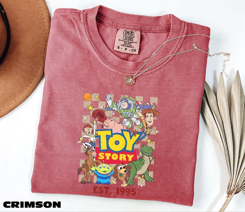 A red t-shirt with a cartoon character design and the text "Toy Story" printed on it, along with a necklace and a hat.