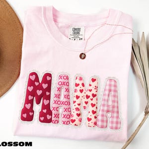 A pink t-shirt with the word "MAMA" printed on it, along with a necklace and a hat.