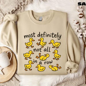 a beige sweatshirt with a humorous text printed on it, along with a mug and some decorative elements such as snowflakes and a branch.