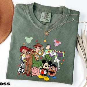 A green t-shirt with a cartoon character design featuring characters from the Toy Story franchise, including Woody, Buzz Lightyear, Timmy, and others.