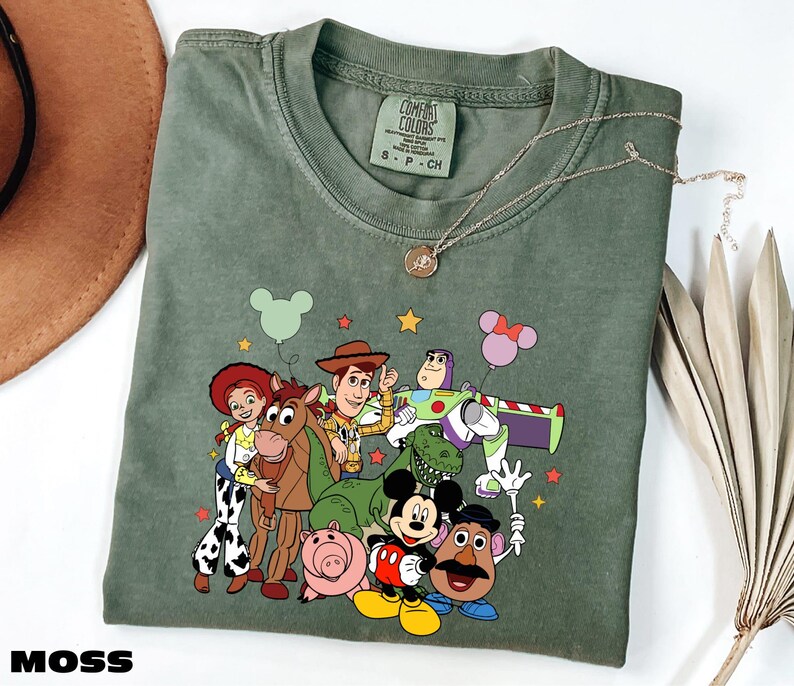A green t-shirt with a cartoon character design featuring characters from the Toy Story franchise, including Woody, Buzz Lightyear, Timmy, and others.