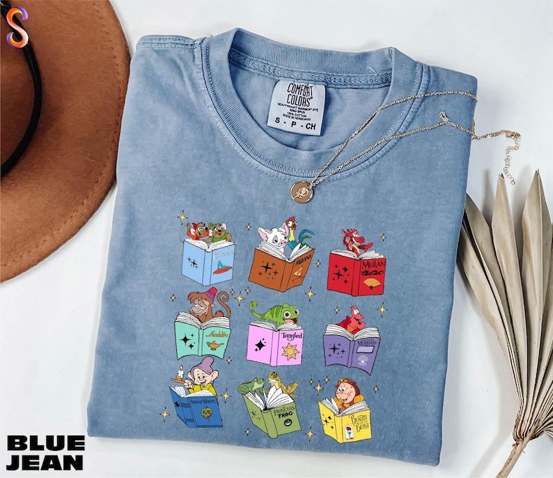 A blue denim t-shirt with a colorful graphic design of various cartoon characters and books, along with a necklace and a hat.