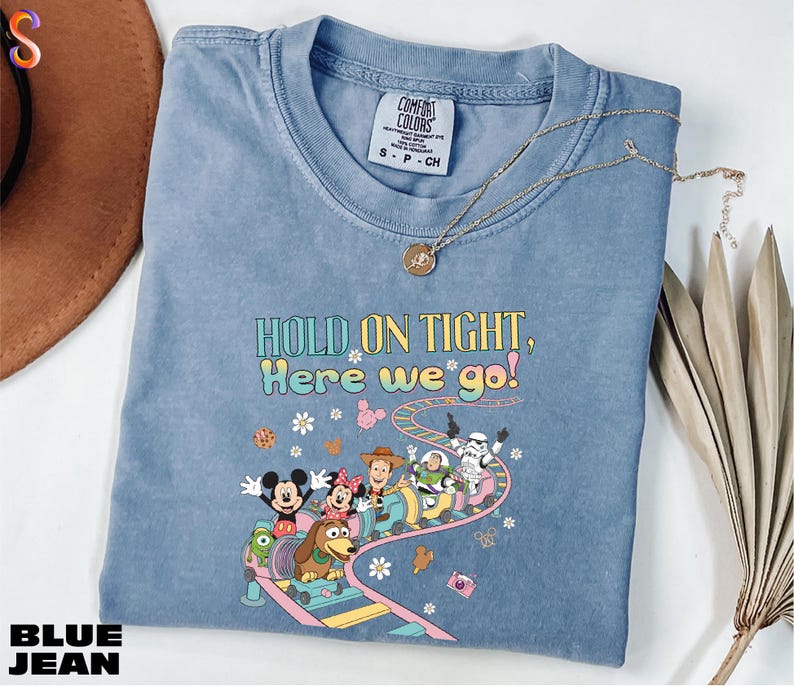 A blue denim t-shirt with a cartoon character design and text printed on it, along with a necklace and some decorative leaves.