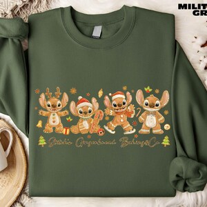 A green sweatshirt with a graphic design featuring four cartoon characters, likely from a children's television show or movie, along with various holiday-themed elements such as snowflakes, Christmas trees, and gingerbread cookies.