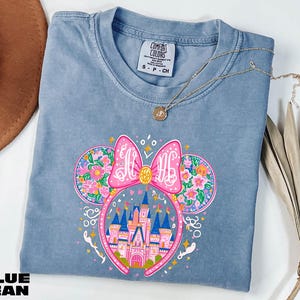 A blue t-shirt with a colorful graphic design featuring a castle and flowers, along with a necklace and a hat.