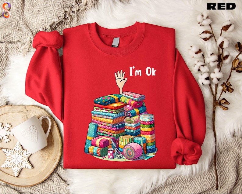 May include: Red sweatshirt with a white hand and the text "I'm Ok" printed on the front. The hand is holding a stack of colorful fabric scraps.