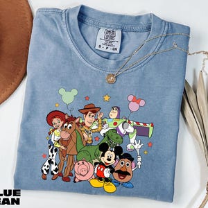 A blue t-shirt with a cartoon character design featuring characters from the Toy Story franchise, including Woody, Buzz Lightyear, and other beloved characters.