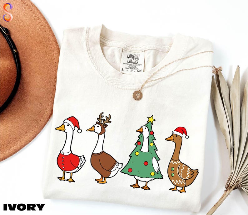 A white t-shirt with a Christmas-themed design featuring four cartoon ducks in festive attire, including Santa hats and Christmas trees.