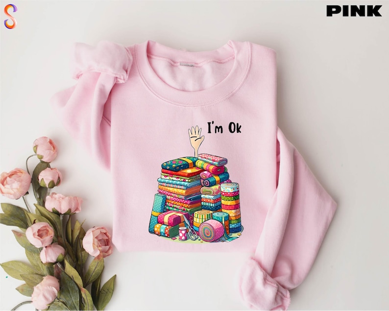 May include: Pink sweatshirt with a graphic of a pile of colorful fabric scraps and the text "I'm Ok".