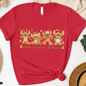 A red t-shirt with a graphic design featuring four cartoon characters, likely from the Disney movie Lilo & Stitch, along with the text "Stitch's Gingerbread Co."