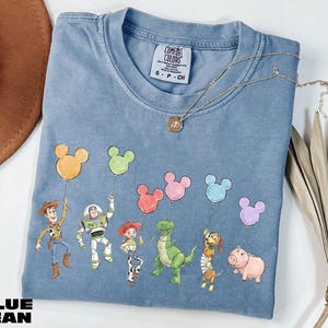 A blue t-shirt with a cartoon character design featuring a group of characters from the Toy Story movie, including Woody, Buzz Lightyear, and other beloved characters.