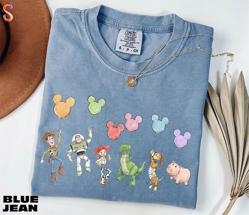 A blue t-shirt with a cartoon character design featuring a group of characters from the Toy Story movie, including Woody, Buzz Lightyear, and other beloved characters.