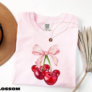 a pink shirt with a pink bow and two cherries on it