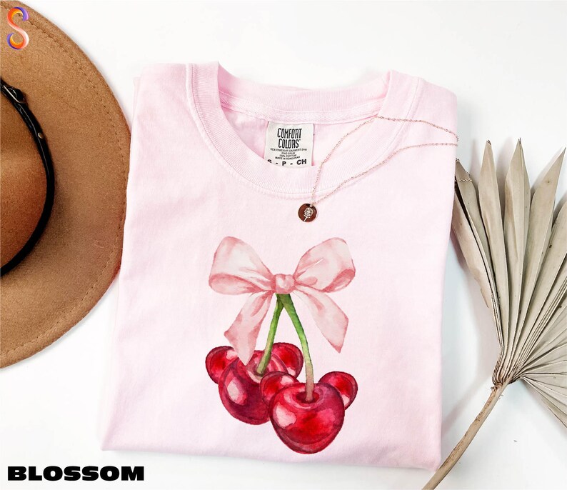 a pink shirt with a pink bow and two cherries on it